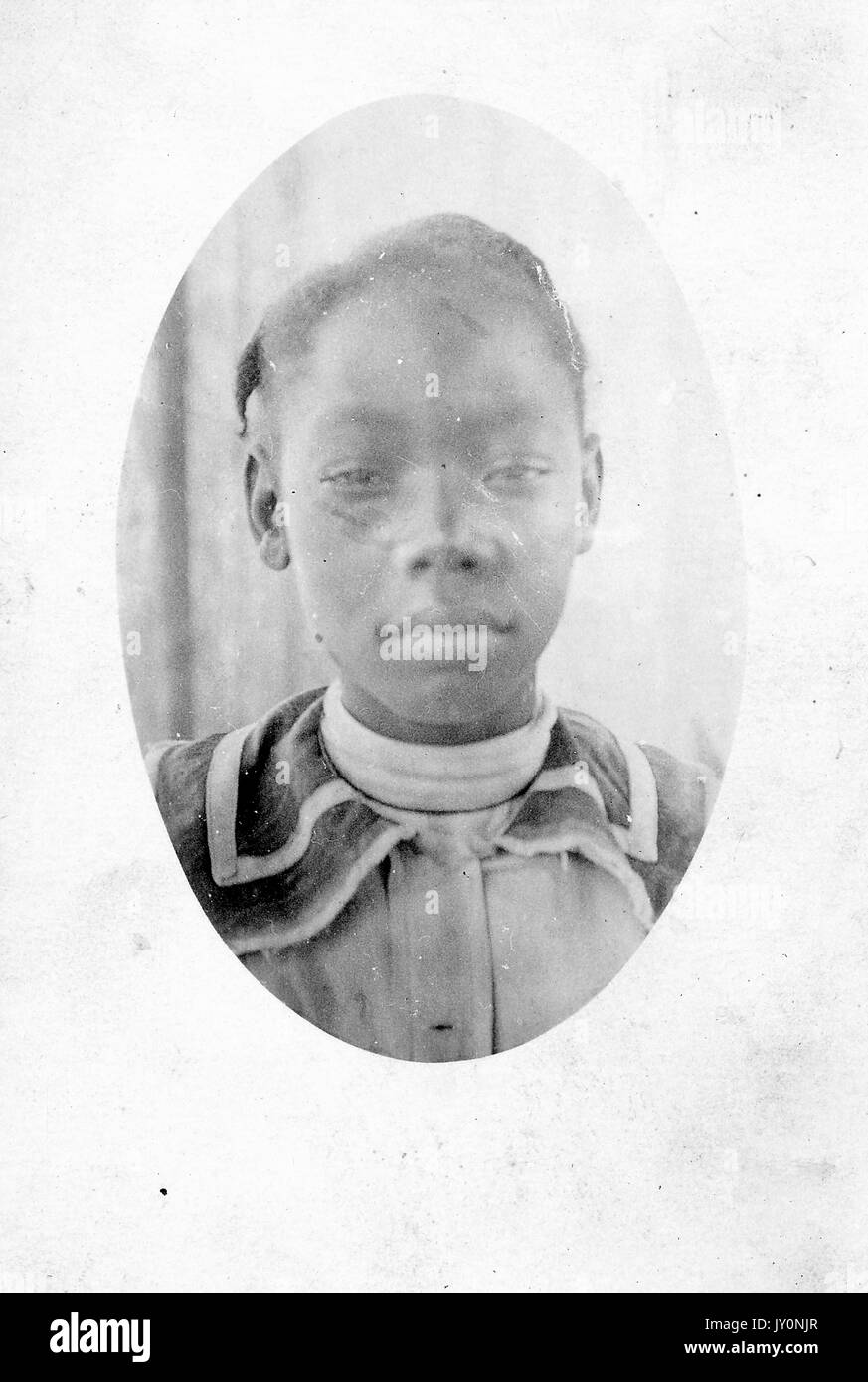 Oval headshot of a young African American woman, wearing a white turtleneck under a collared coat, with a serious facial expression, 1920. Stock Photo