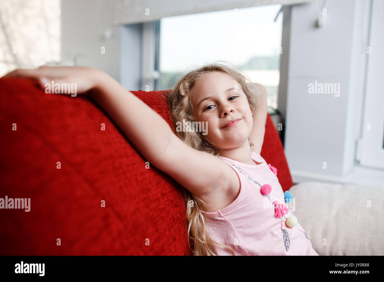 Happy 6 year old girl is sitting on red chair in his room. Stock Photo