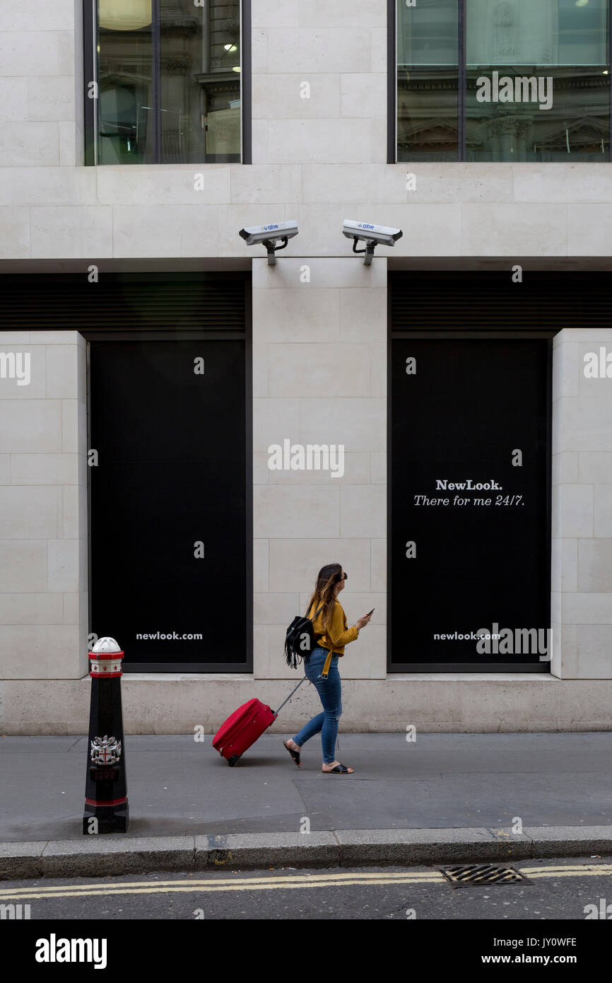 A Londoner walks beneath two CCTV cameras in the City of London, one of