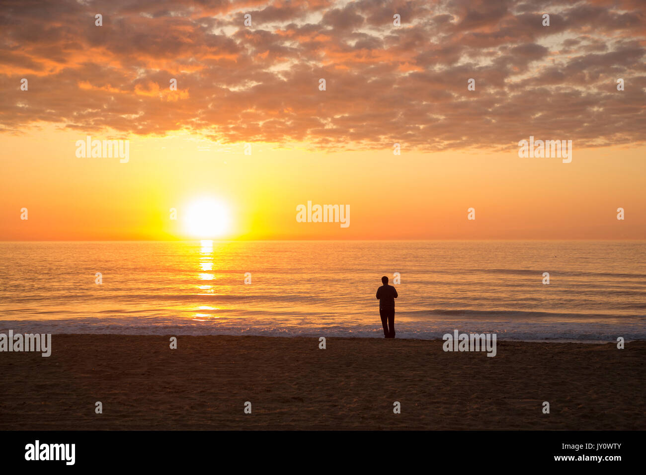 Silhouette of man standing on ocean beach at sunset Stock Photo