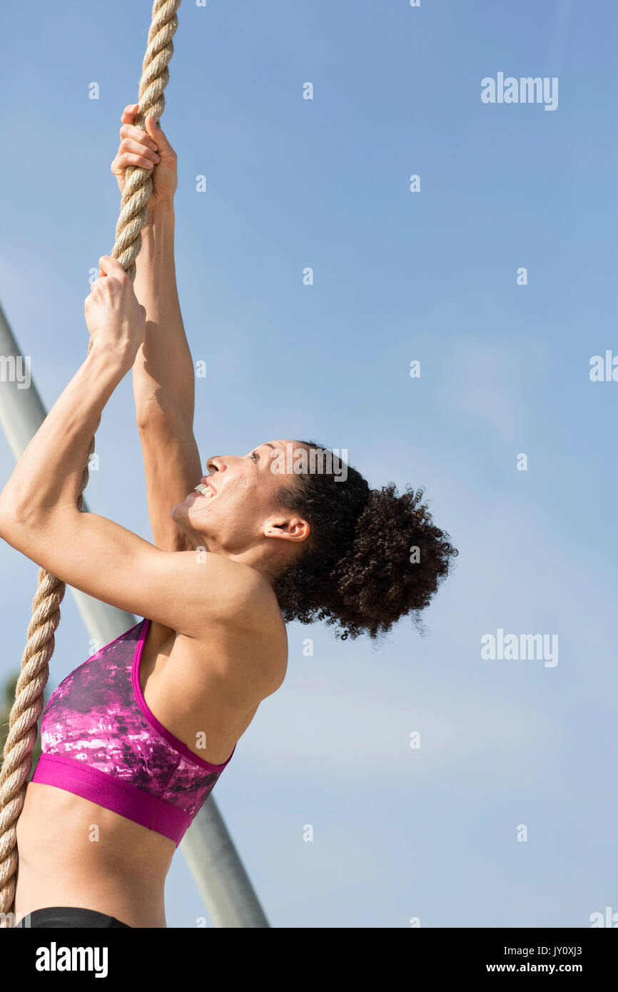 Mixed Race woman climbing rope outdoors Stock Photo