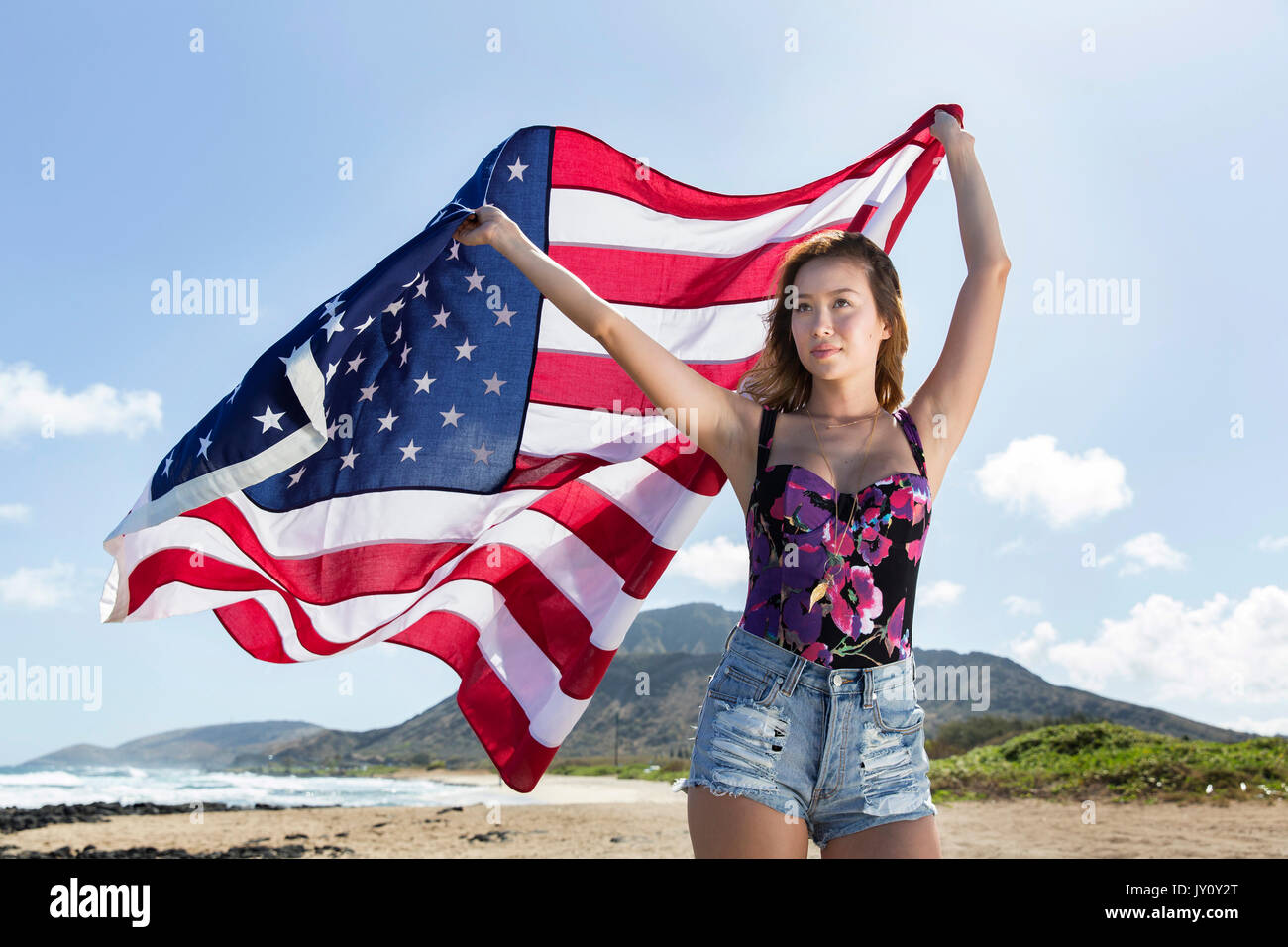 Mixed Race woman holding American flag on beach Stock Photo