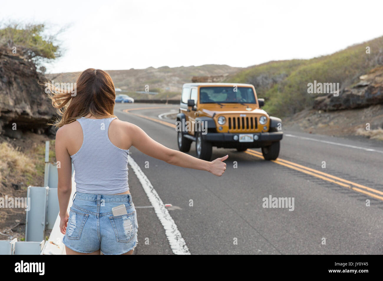 Mixed Race woman hitchhiking on road Stock Photo - Alamy