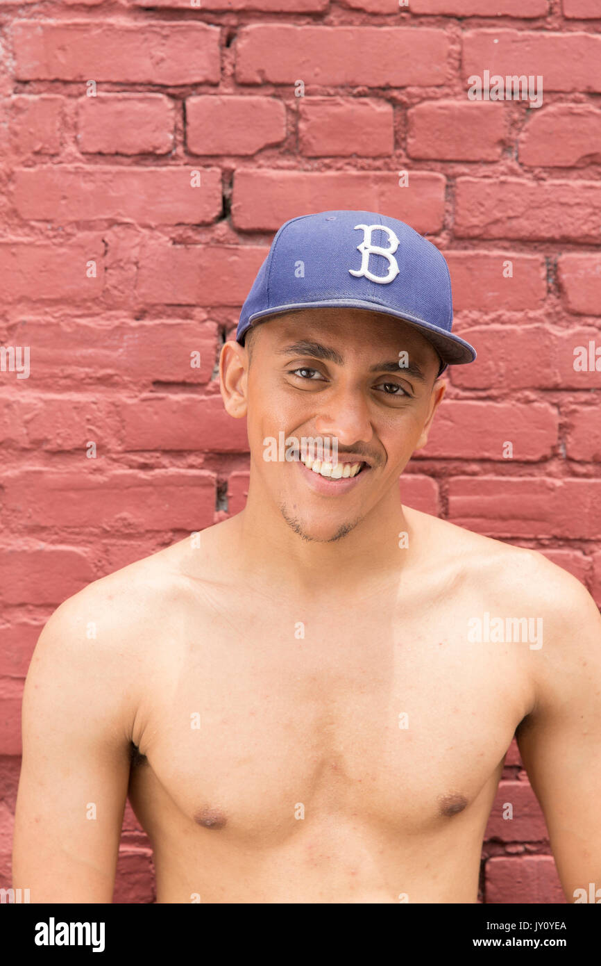 Portrait of shirtless Mixed Race man wearing hat near brick wall Stock Photo