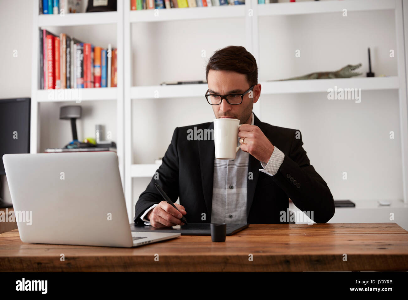 Caucasian businessman using laptop and digital tablet drinking coffee Stock Photo