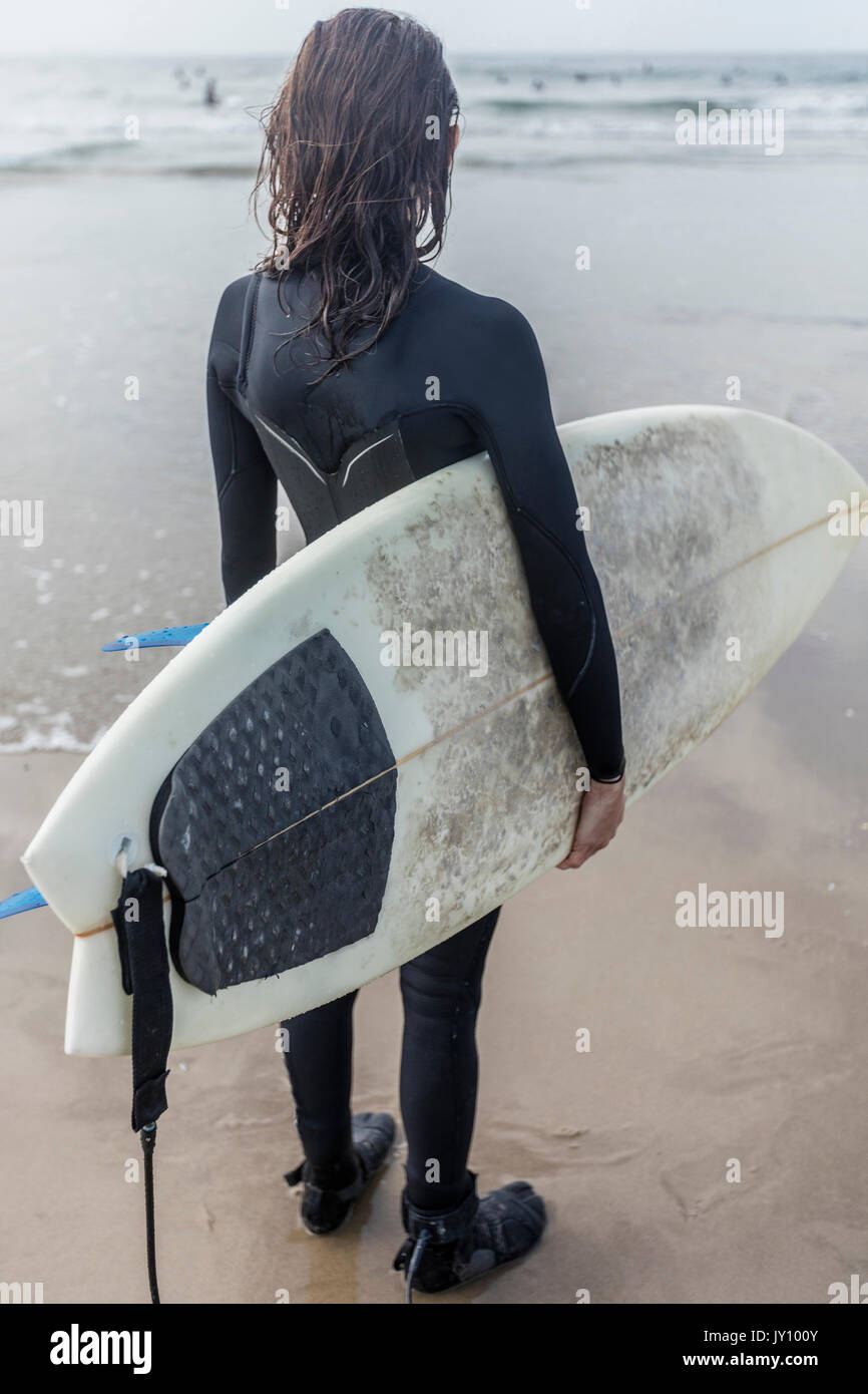 Caucasian woman standing on beach holding surfboard Stock Photo