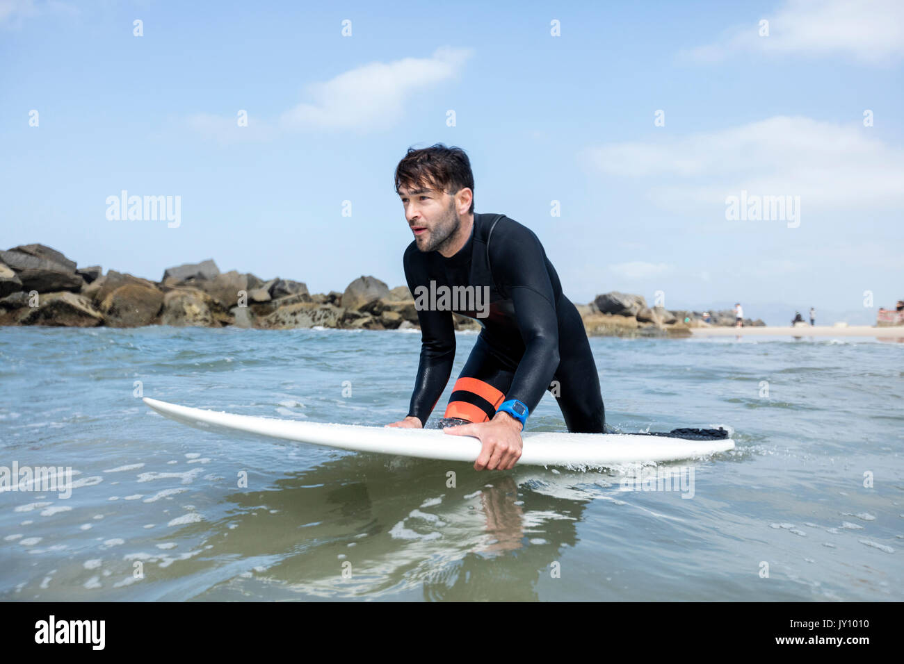 Caucasian man wading in ocean holding surfboard Stock Photo