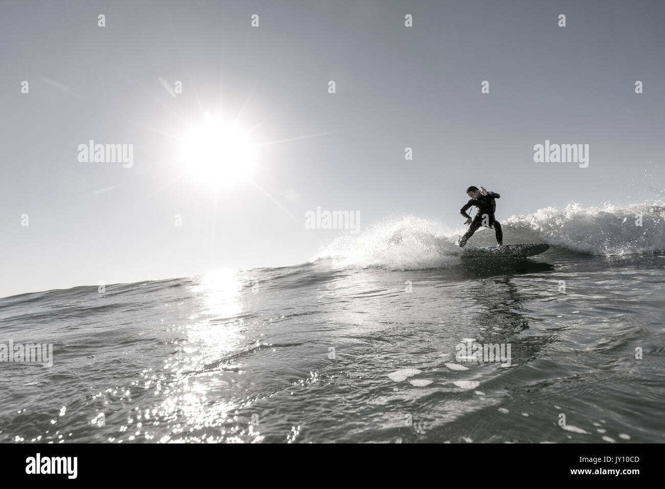 Distant Caucasian man surfing in sunny ocean Stock Photo