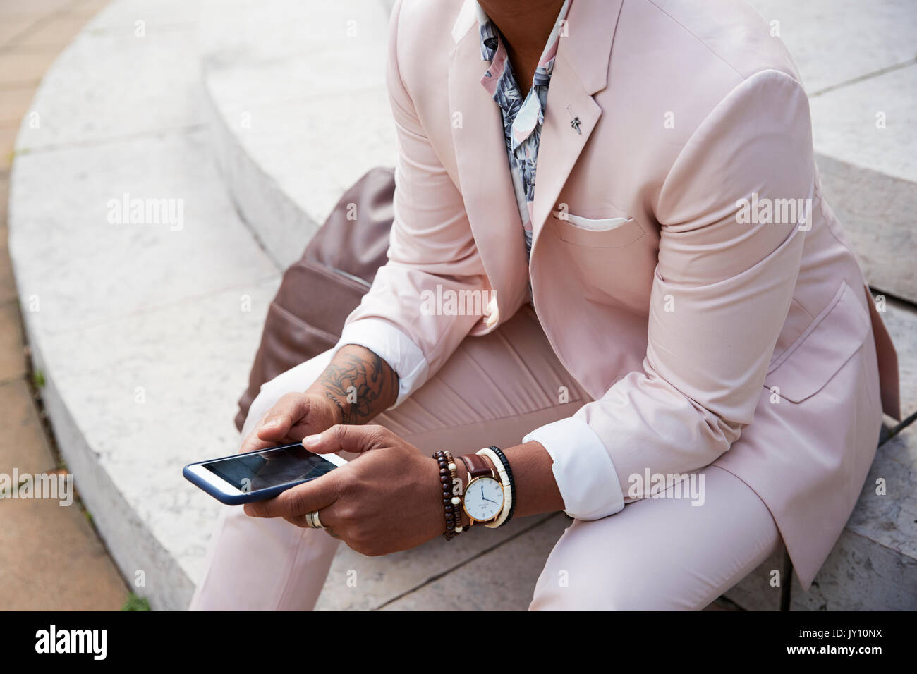 Mid section of a man in pink suit sitting using smartphone Stock Photo