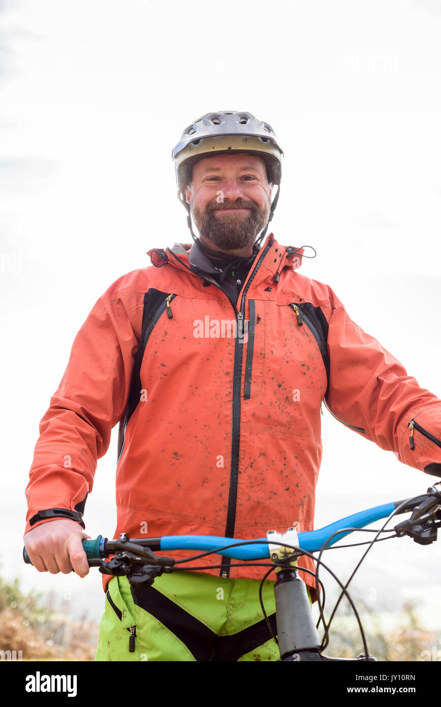Portrait of smiling Caucasian man splattered in mud holding bicycle Stock Photo