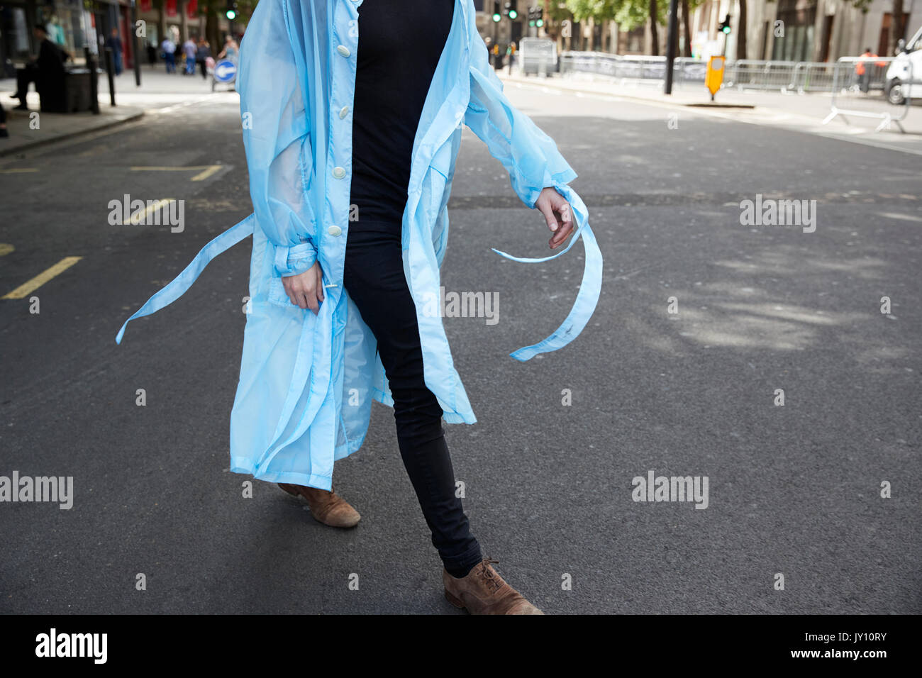 Man in black trousers and blue sheer coat walking in street Stock Photo