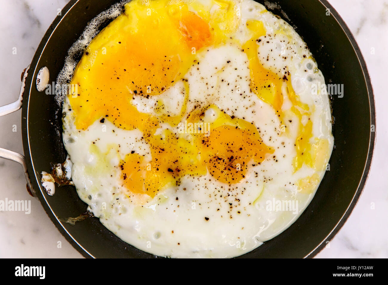 Fried eggs with pepper on top in a frying pan, top view. Stock Photo