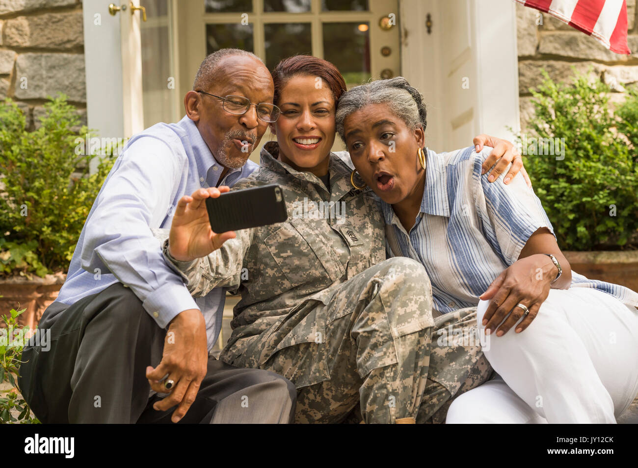 Soldier sitting on front stoop with parents and posing for cell phone selfie Stock Photo