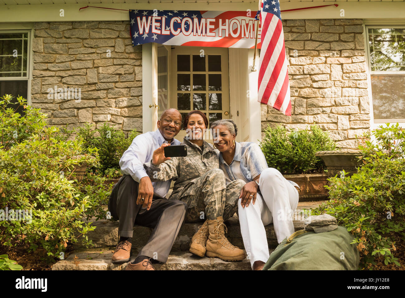Soldier and parents sitting on front stoop posing for cell phone selfie Stock Photo