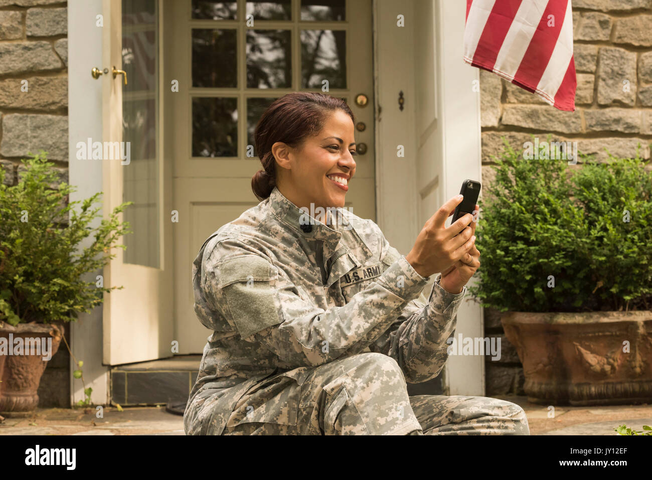 Smiling African American soldier sitting on front stoop texting on cell phone Stock Photo
