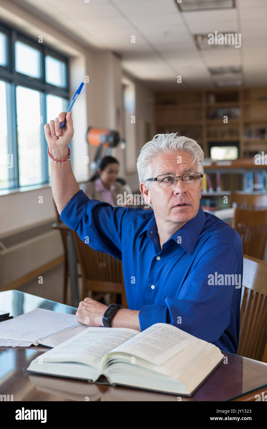 Older man in library raising hand and asking question Stock Photo