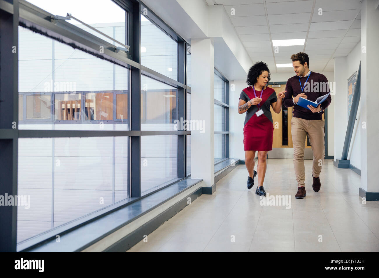 Two teachers are walking and talking together down the school hall ...