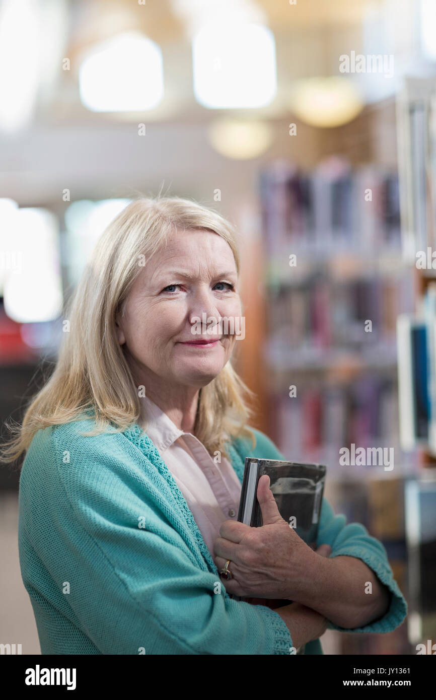 Smiling Caucasian woman holding book in library Stock Photo