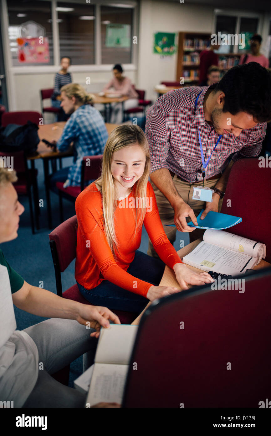 Students are laughing as they work on computers together. There is a teacher leaning over their shoulder, helping them with their work. Stock Photo