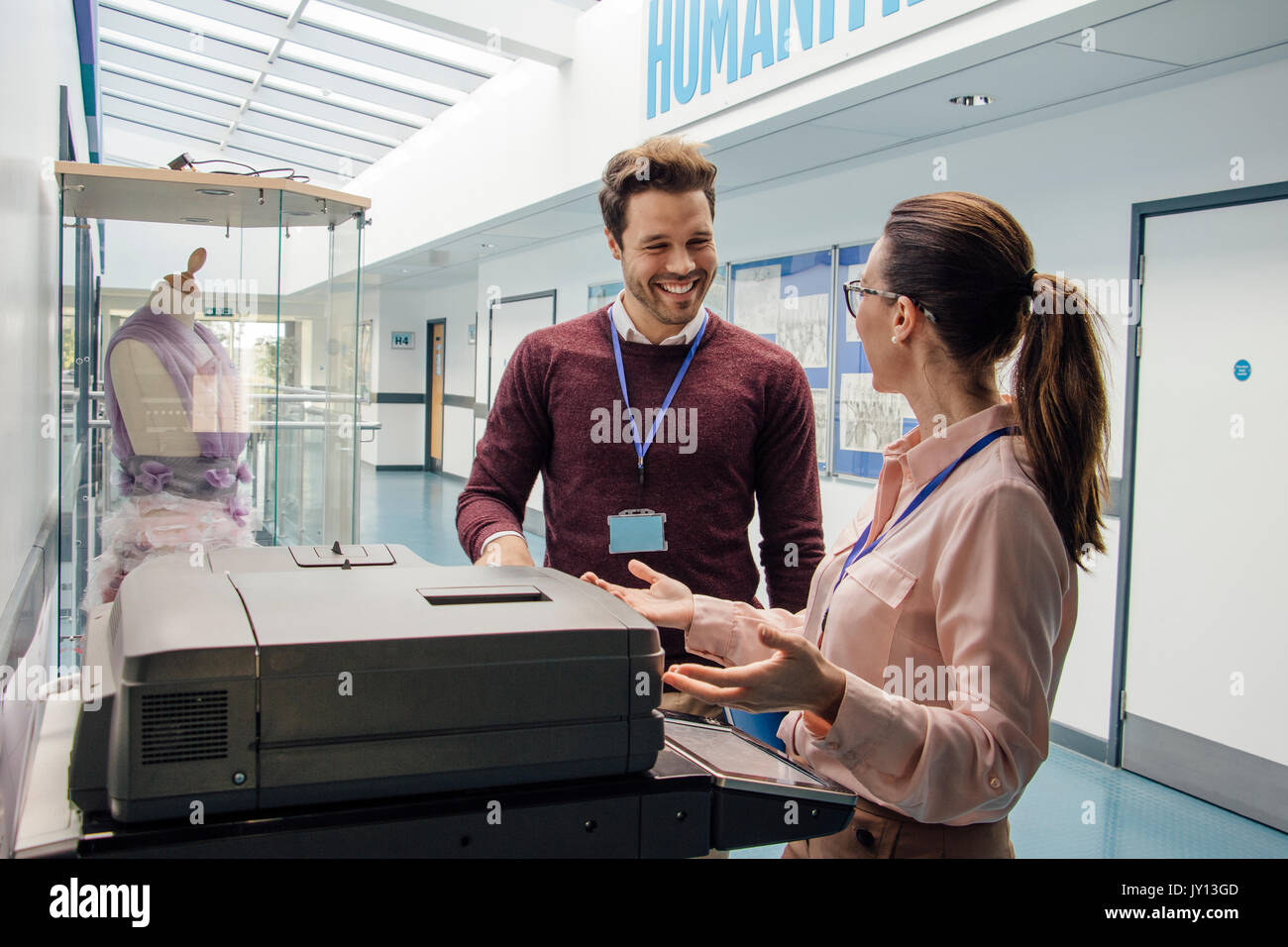 Two teachers are talking while standing at a printer in the school hall. Stock Photo