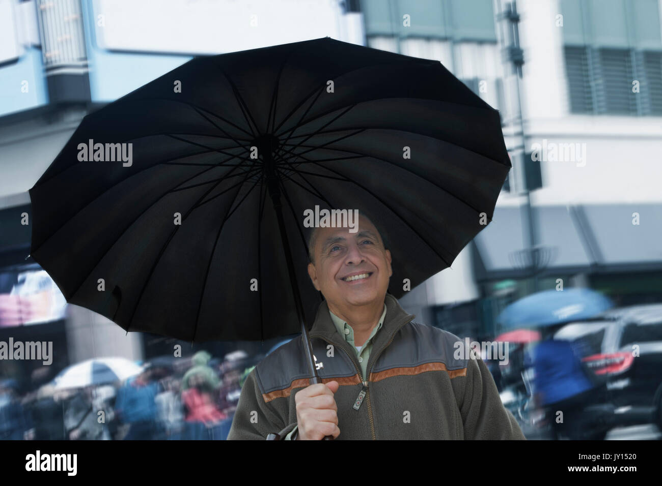 Smiling Hispanic man holding umbrella in city Stock Photo