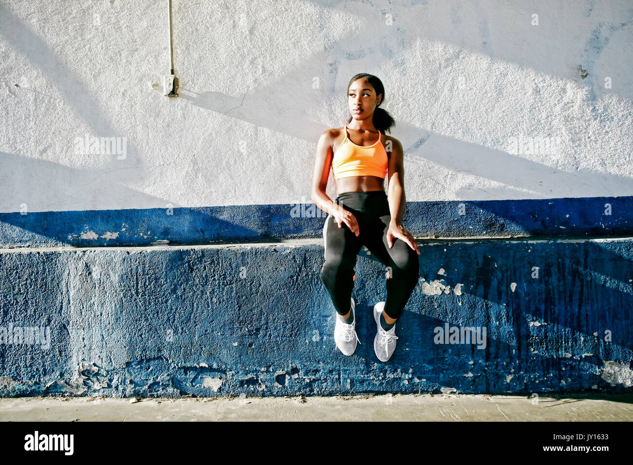 Mixed Race woman sitting on ledge of urban wall Stock Photo