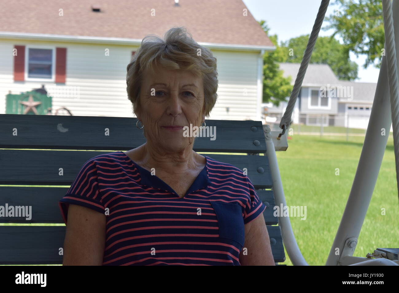 Elderly woman sitting on a swing in her backyard Stock Photo