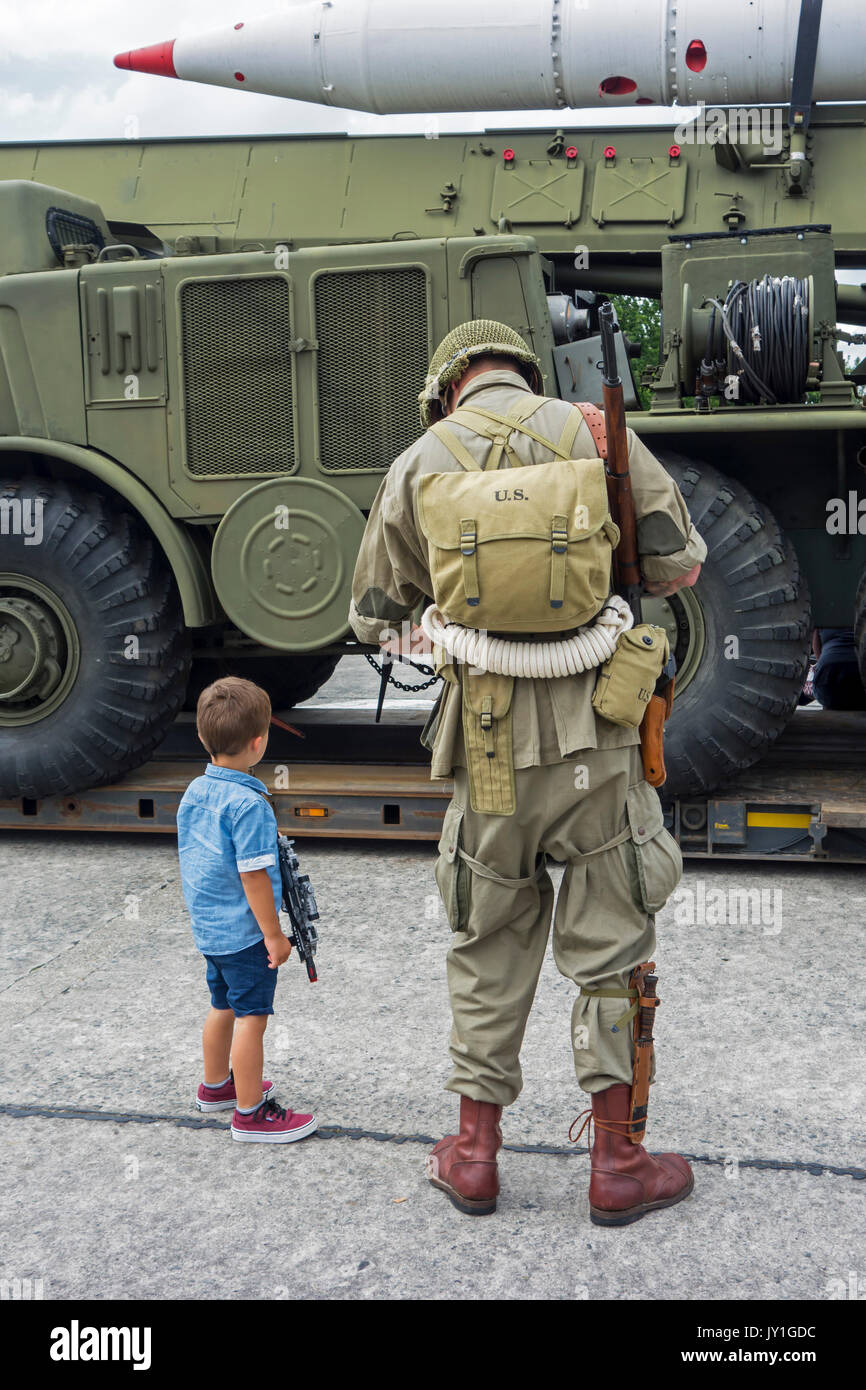 Little boy with toy gun and WW2 reenactor in US soldier outfit looking at missile truck at World War Two militaria fair Stock Photo