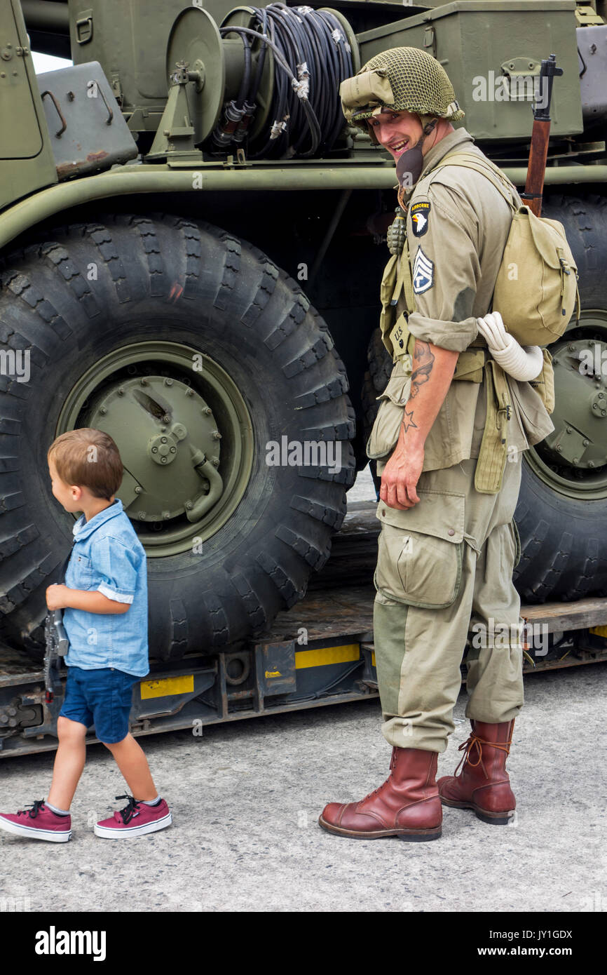 Little boy with toy gun and WW2 reenactor in US soldier outfit looking at missile truck at World War Two militaria fair Stock Photo