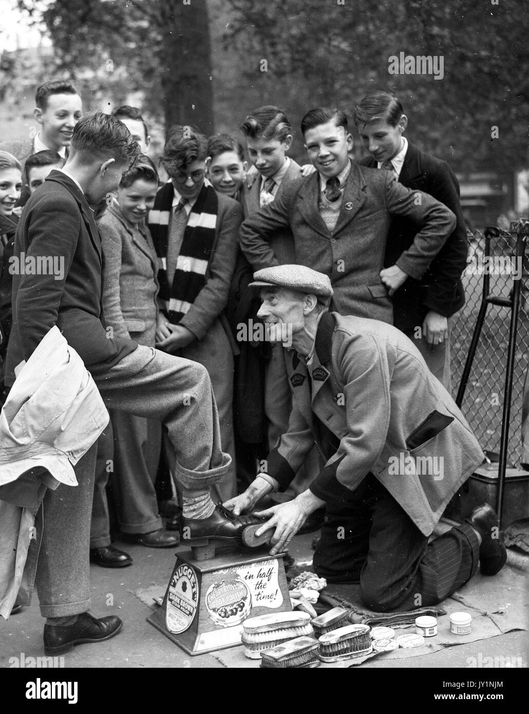 Disabled shoe shine man with only one leg polishing school boys shoes on in London 1954 shoeshine man. Stock Photo