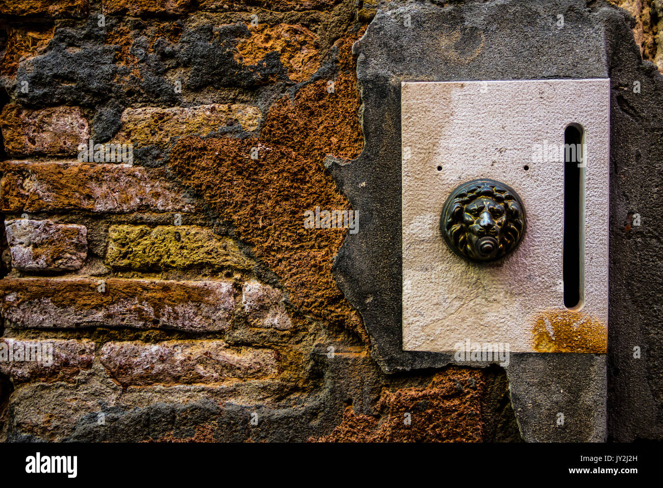 brass doorplate and doorbell in a shape of a lion's head on an old, cracked brick wall , Venice, Italy Stock Photo