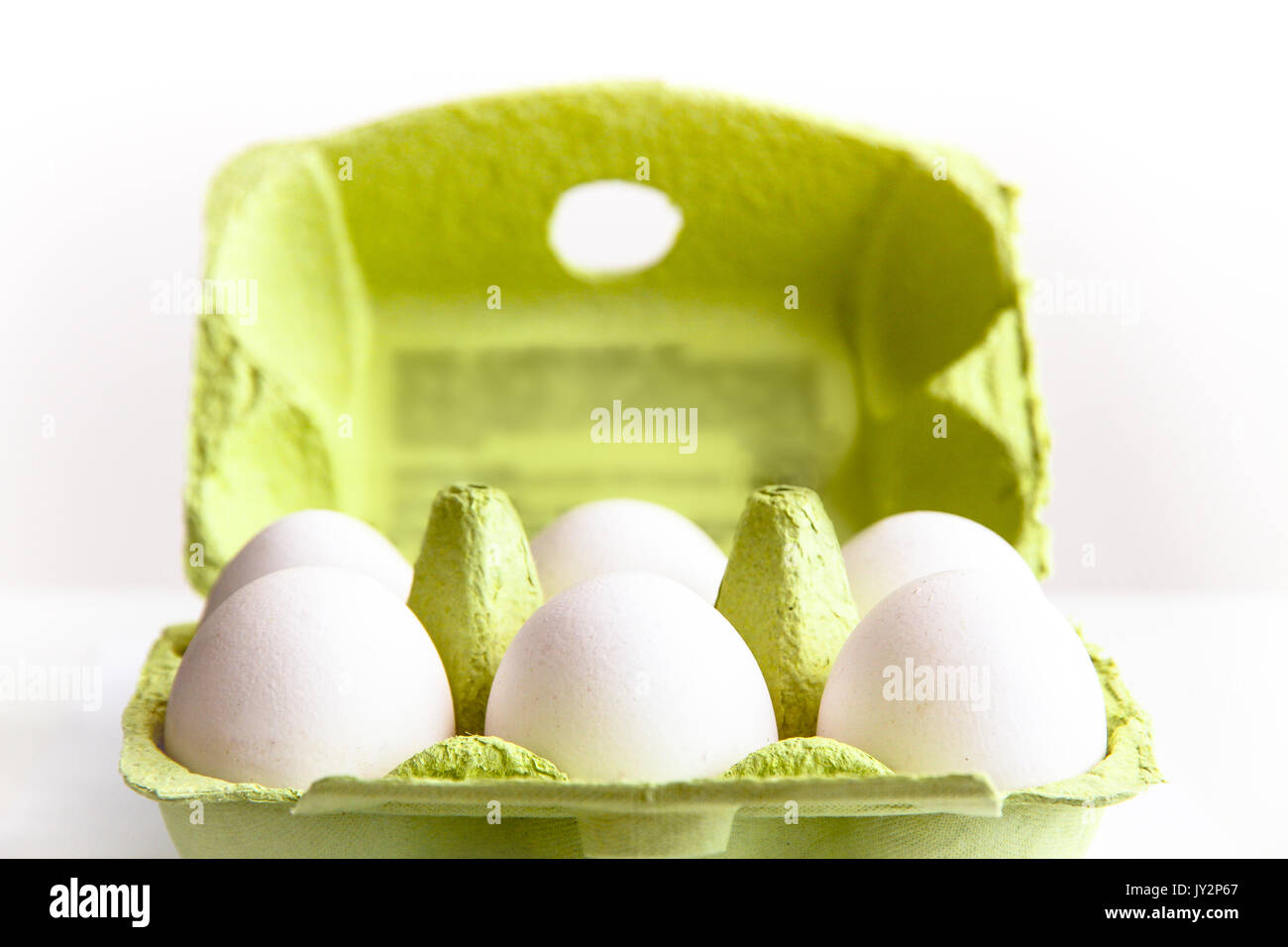 Six white eggs in a open green package, viewed from the top/side, against a white background closeup. Stock Photo