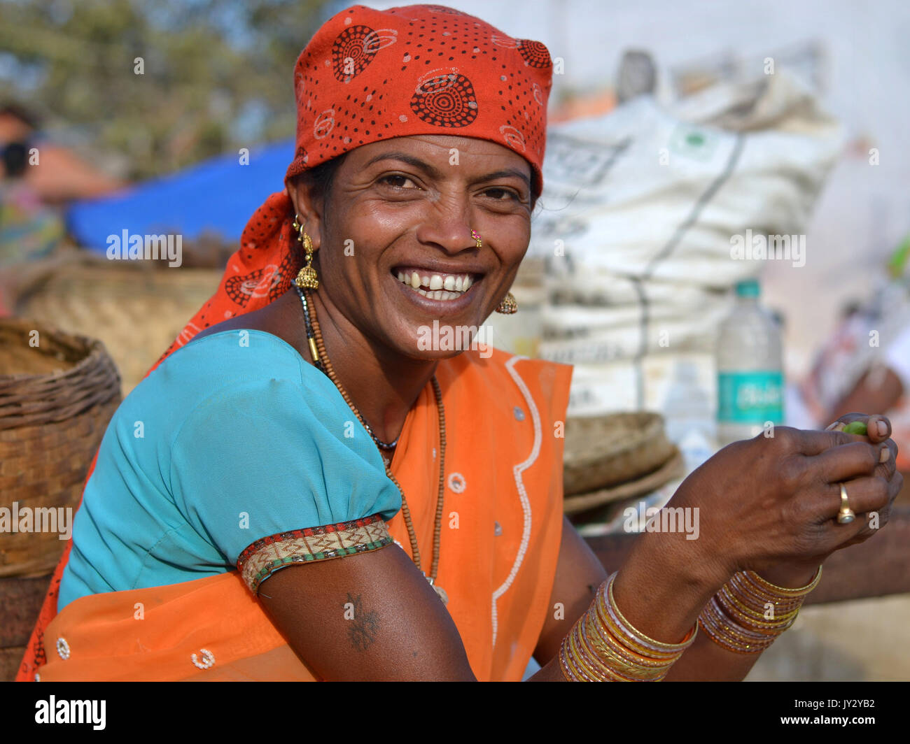 Smiling Indian Adivasi woman peels vegetable with both hands. Stock Photo