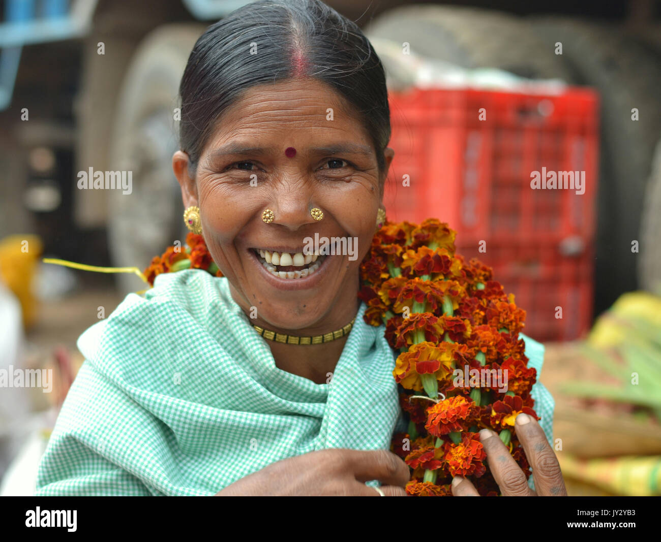 Smiling and laughing Indian Adivasi woman carries a flower garland over her left shoulder and poses for the camera. Stock Photo
