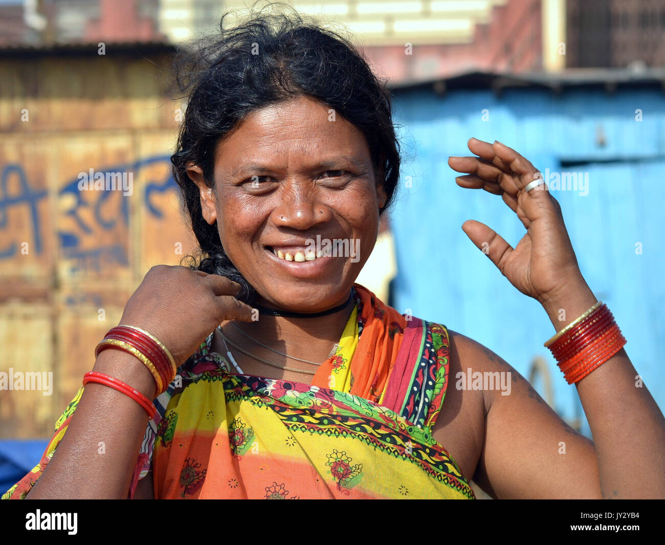 Smiling and laughing Indian Adivasi woman does her hair with both hands and shows her bangles. Stock Photo