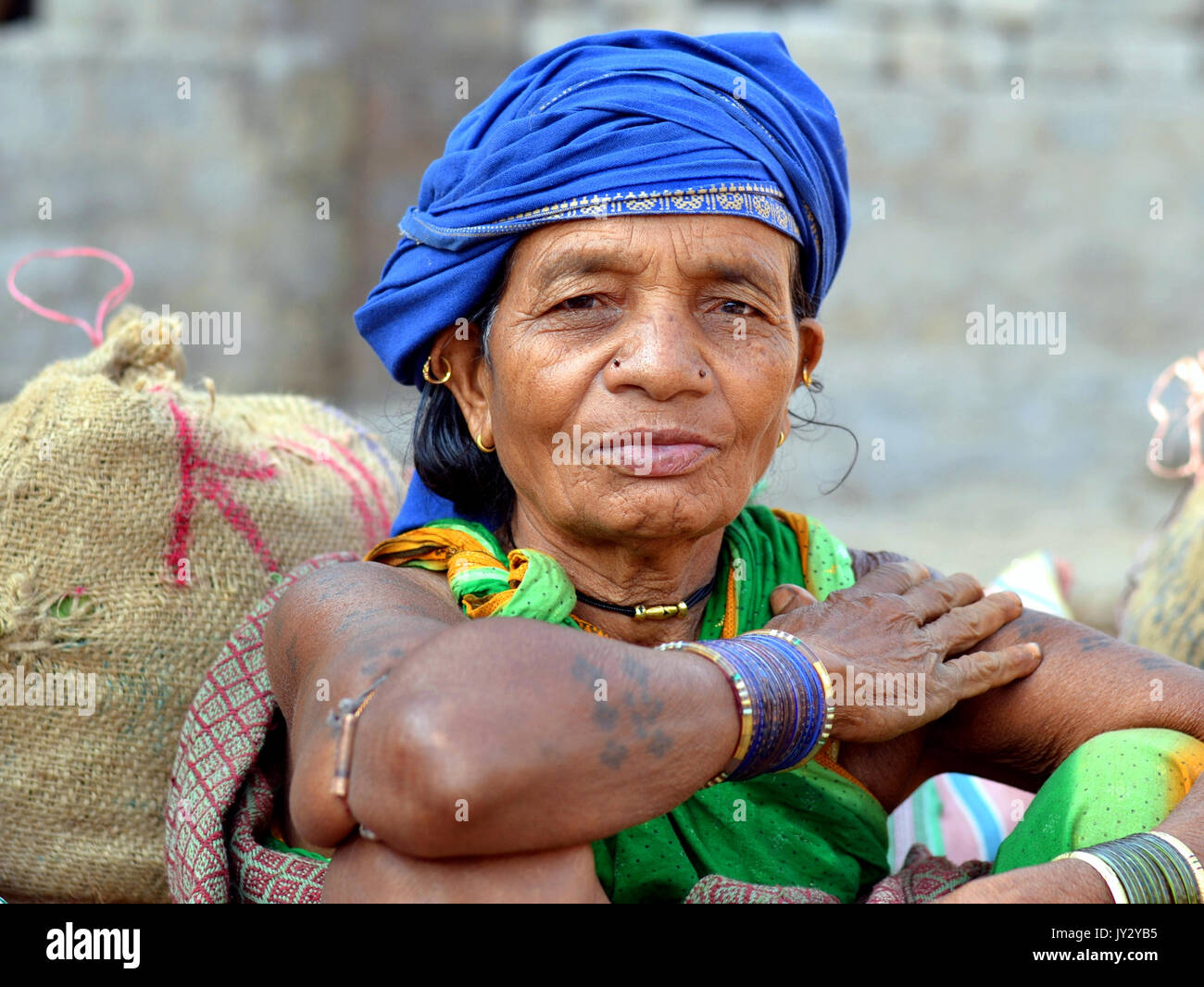 Elderly Indian Adivasi woman with blue head wrap and blue bangles poses for the camera. Stock Photo