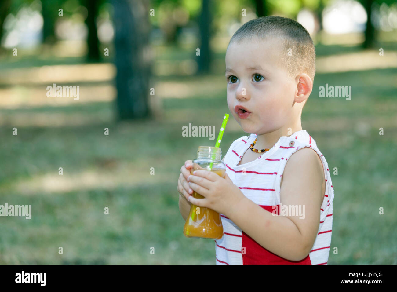 Portrait of a cute little boy outside while drinking juice from a glass bottle in summer Stock Photo