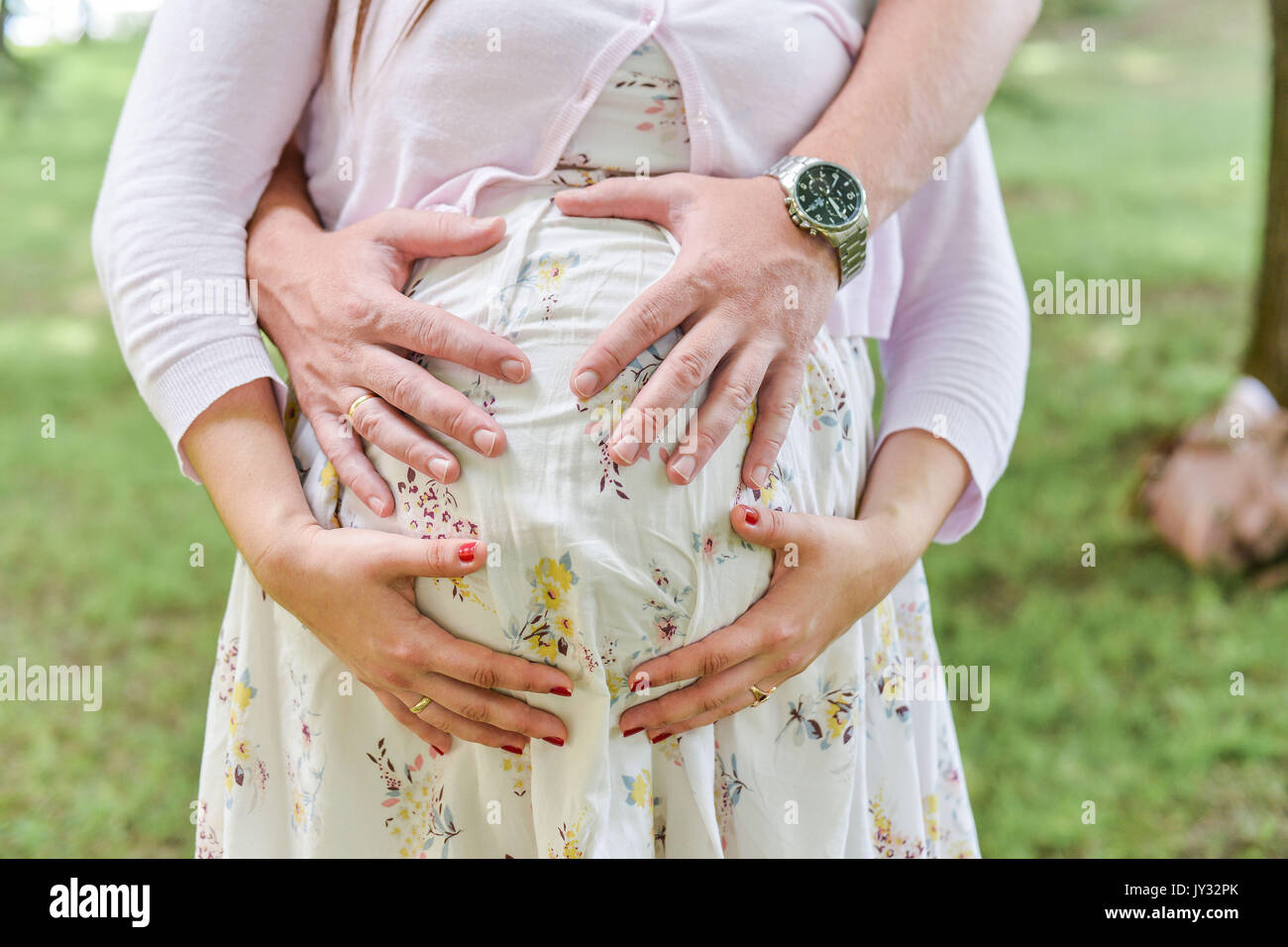 Hands of female male and baby make heart shape cute sign on bare belly ...