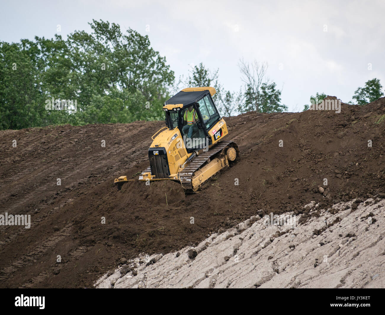 Bulldozer pushing topsoil down side of hill to prepare for seeding and erosion control. Stock Photo