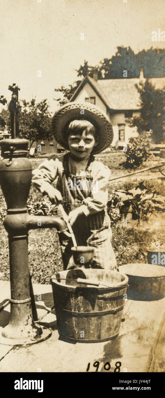 A young boy getting a drink of water from the hand pumped well Stock Photo