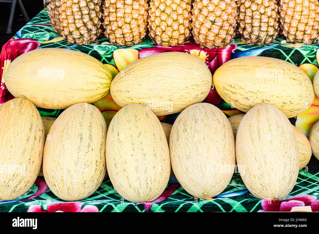 A horizontal photo of yellow melons and pineapples at a farmers market display. Stock Photo