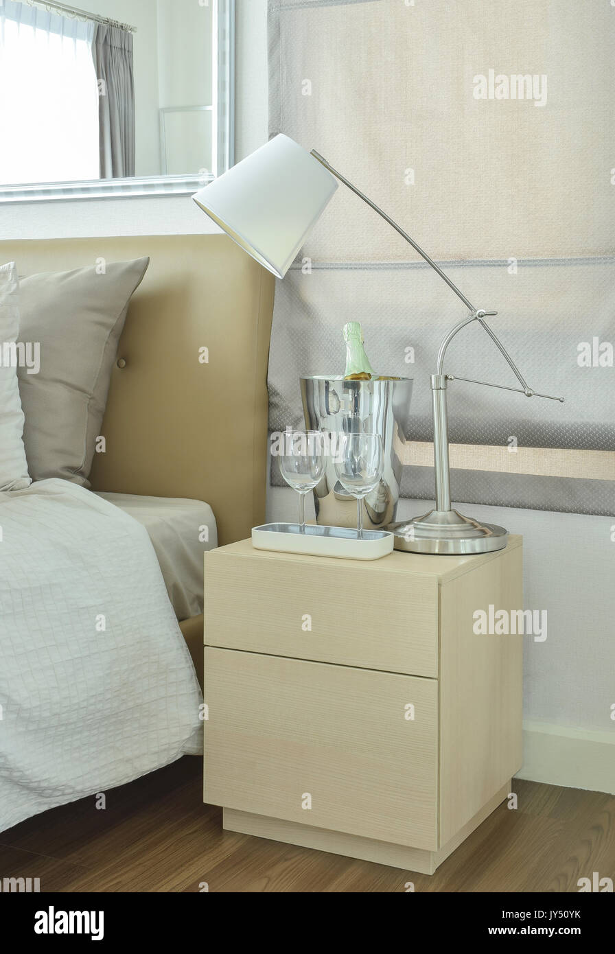 White table lamp with empty glasses and wine bottle on bed side table Stock Photo