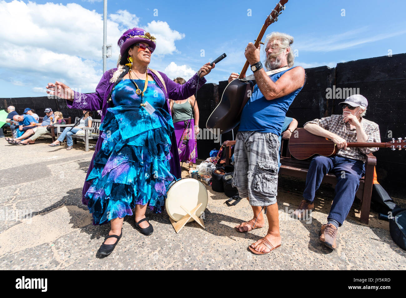 Afro-Caribbean woman holding microphone and recording the lead guitarist from the folk group, Ginny and the Motley Crew playing on the harbour jetty during the yearly Broadstairs Folk week. Stock Photo