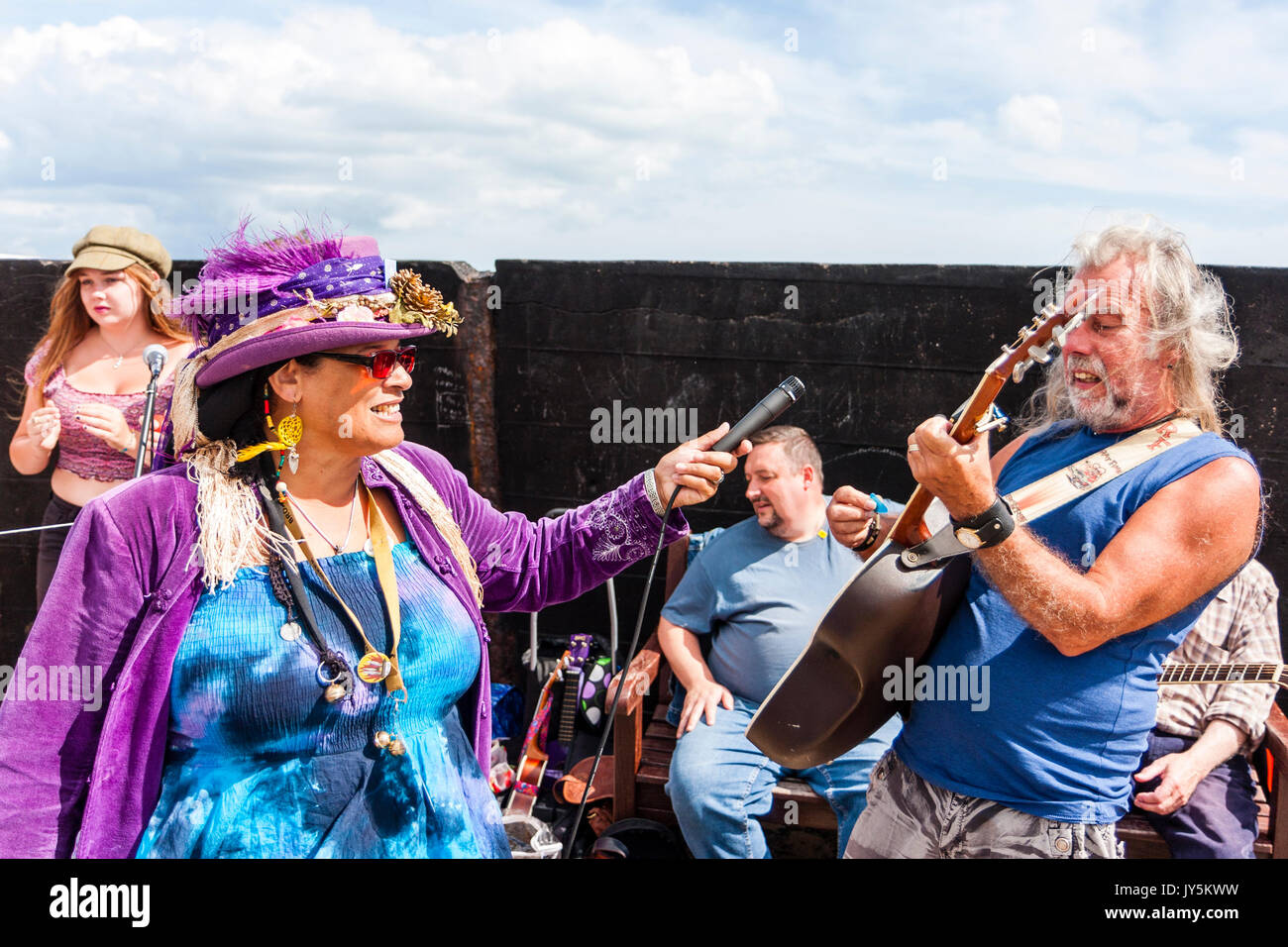 Afro-Caribbean woman holding microphone and recording the lead guitarist from the folk group, Ginny and the Motley Crew playing on the harbour jetty during the yearly Broadstairs Folk week. Stock Photo