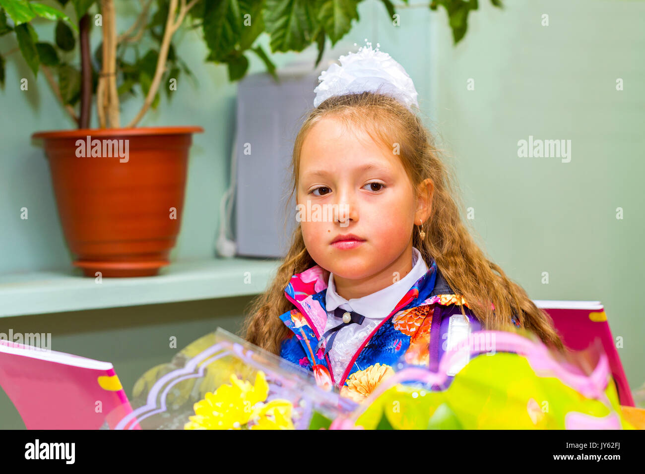 Little first-grader, girl-student in school on knowledge day - 1. September. Student of elementary school in uniform with bows posing in classroom for Stock Photo