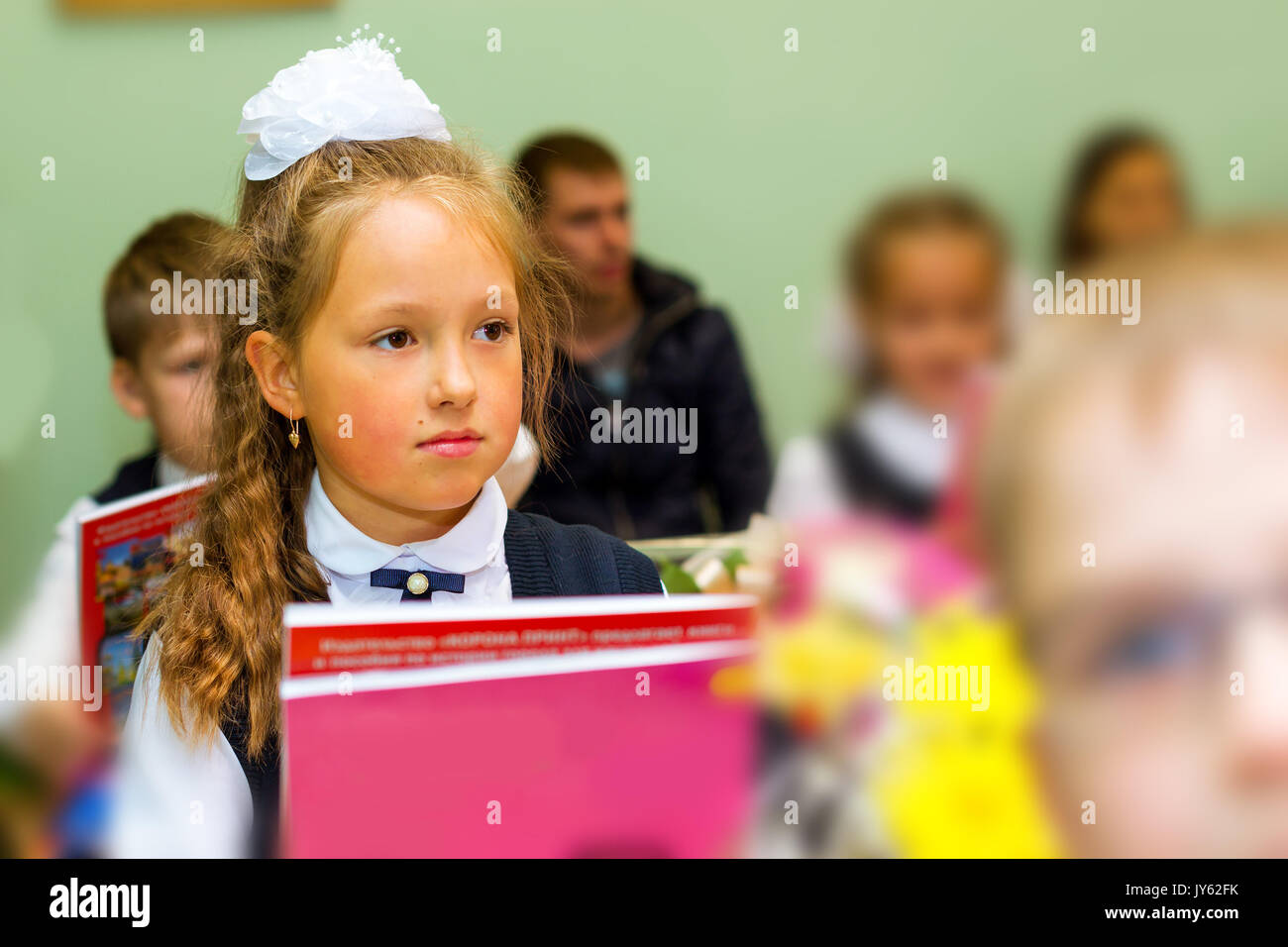 Little first-grader, girl-student in school on knowledge day - 1. September. Student of elementary school in uniform with bows posing in classroom for Stock Photo