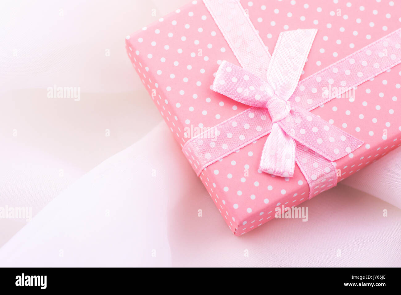 Pink gift box tied with satin ribbon with bow on delicate white fabric ...