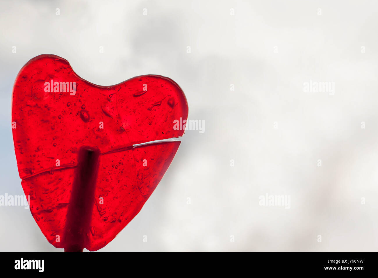 Sweet, transparent and red lollipop heart shape close up in abstract white background Stock Photo