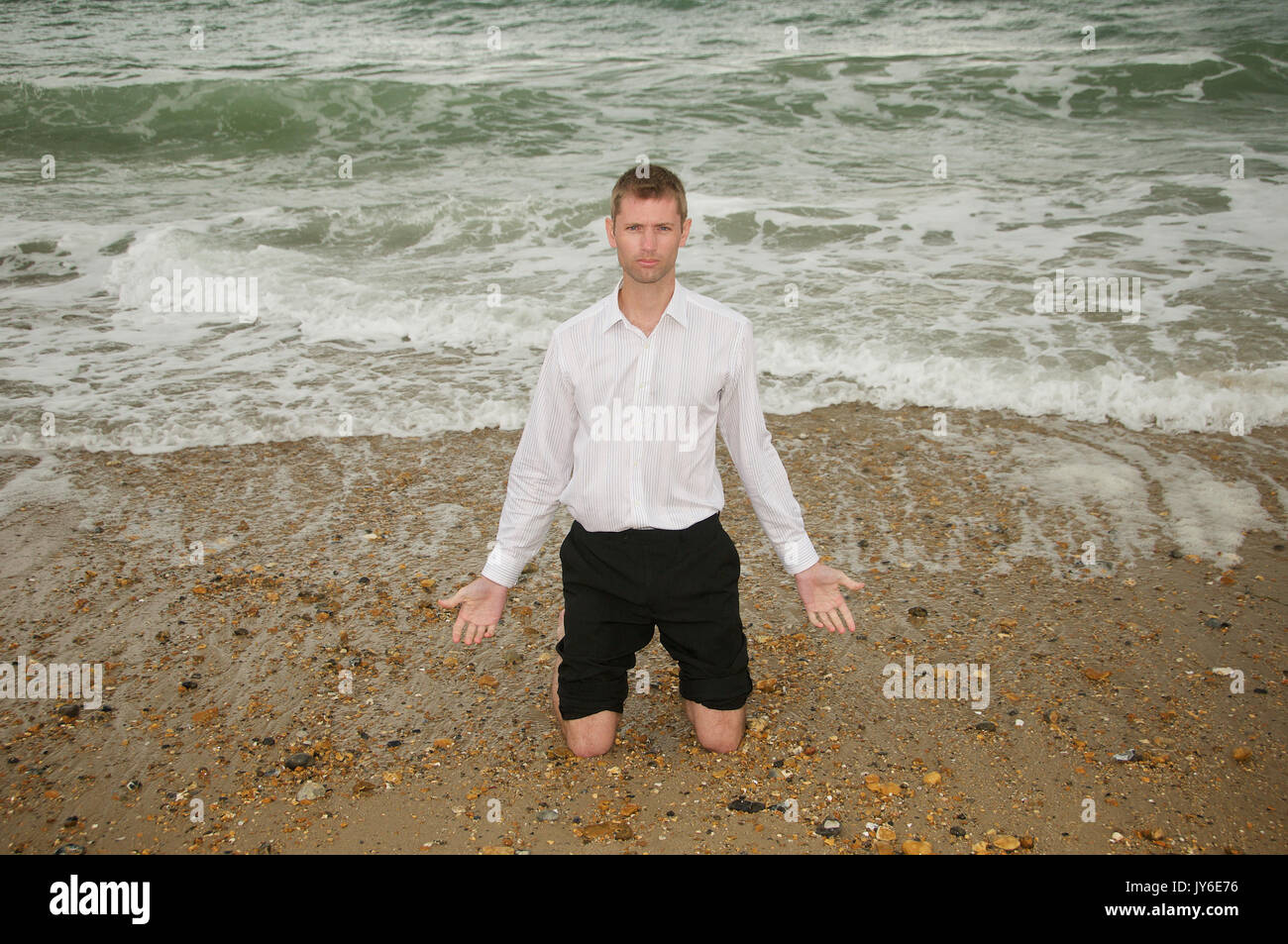 Man on the beach on his knees pleading Stock Photo - Alamy