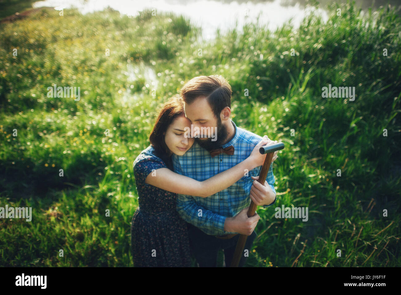 wife affectionately hugging husband on coast of lake in sunny morning Stock Photo